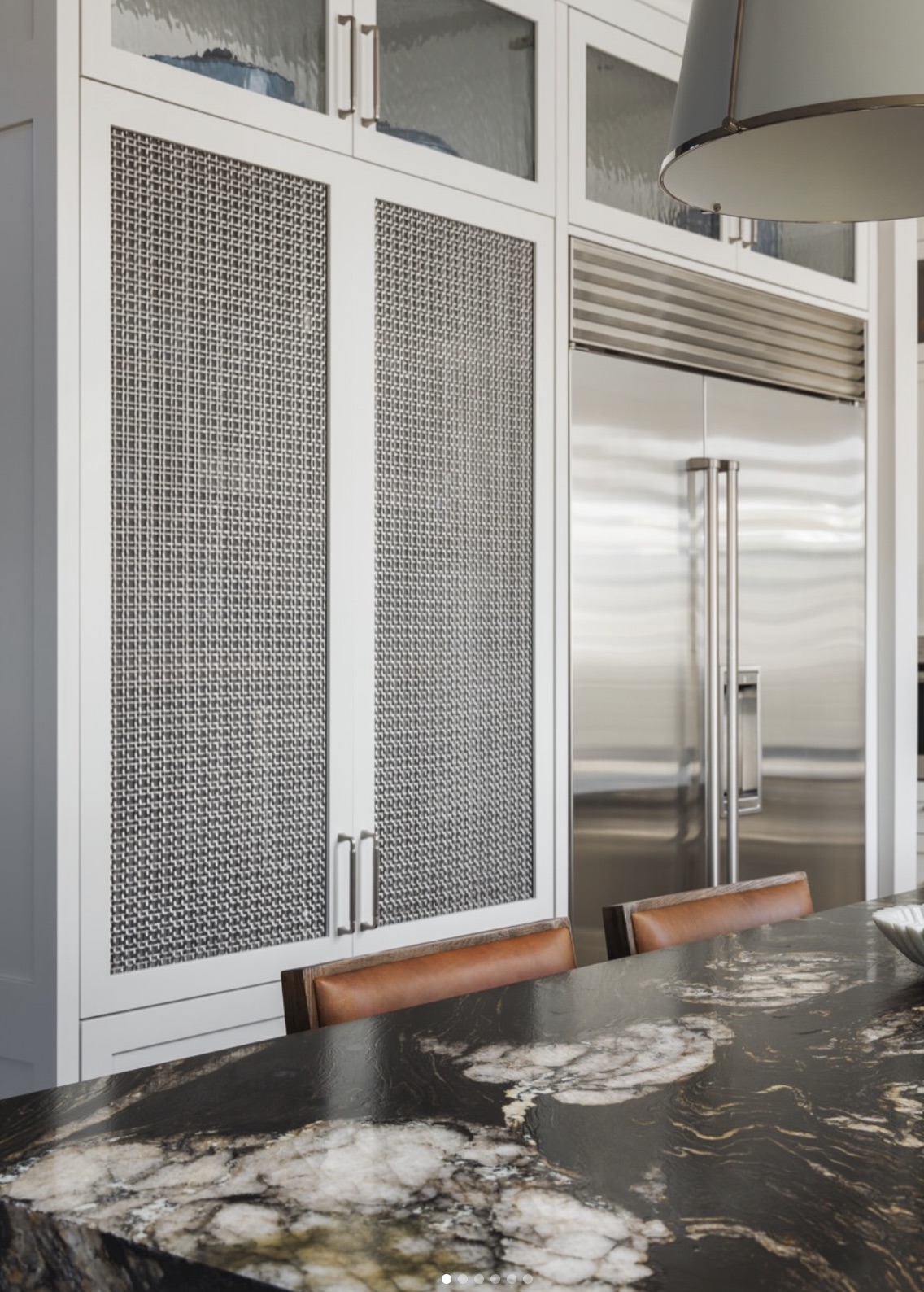 Custom kitchen cabinetry with mesh door inserts and a dramatic stone counter