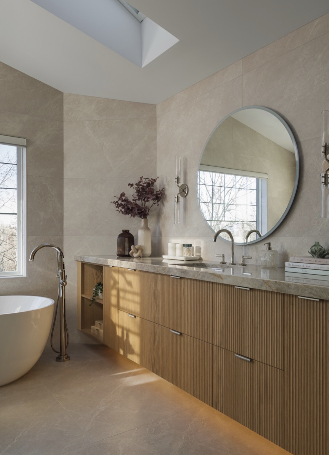 Primary bathroom with a fluted oak vanity, round mirror and freestanding tub
